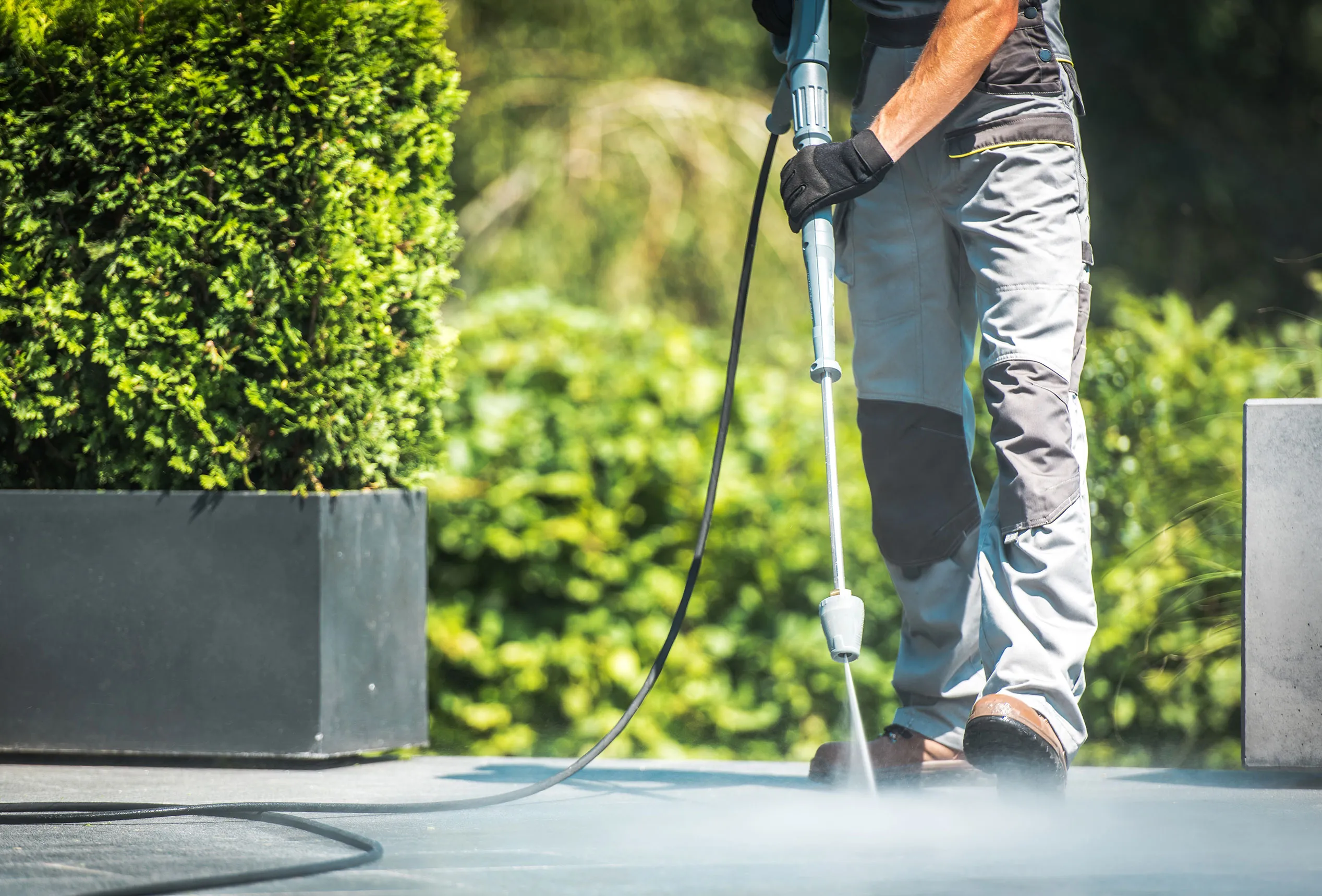 A man using a pressure washer on a driveway.