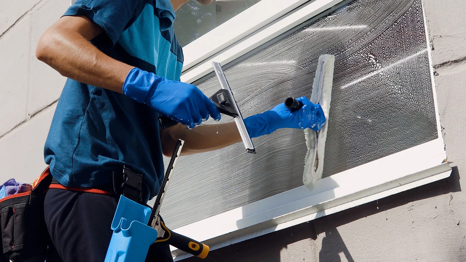 A man in a blue shirt and blue gloves painting a window.
