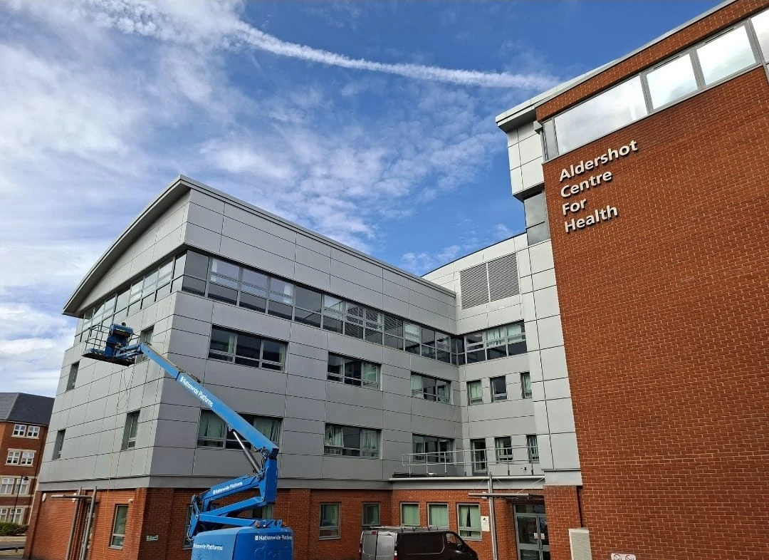Exterior view of the Aldershot Centre for Health, featuring a modern building with a cherry-red brick section and construction equipment.