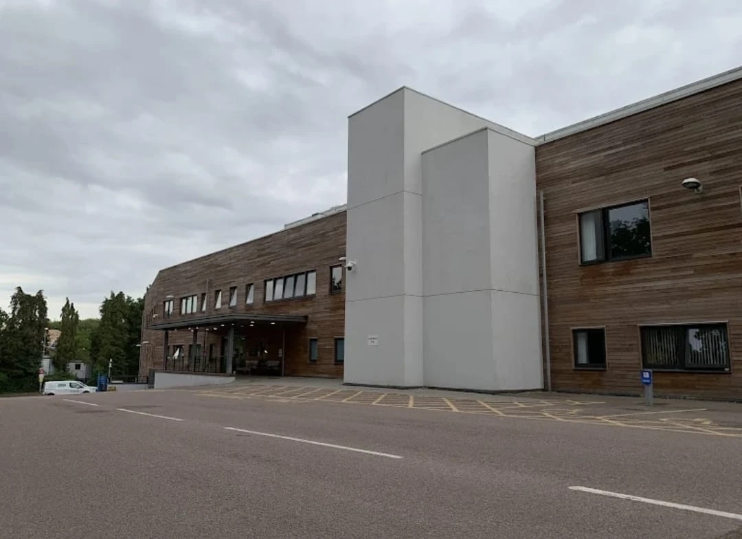 A modern building with a mix of wood and white exterior, situated in a parking area under a cloudy sky.