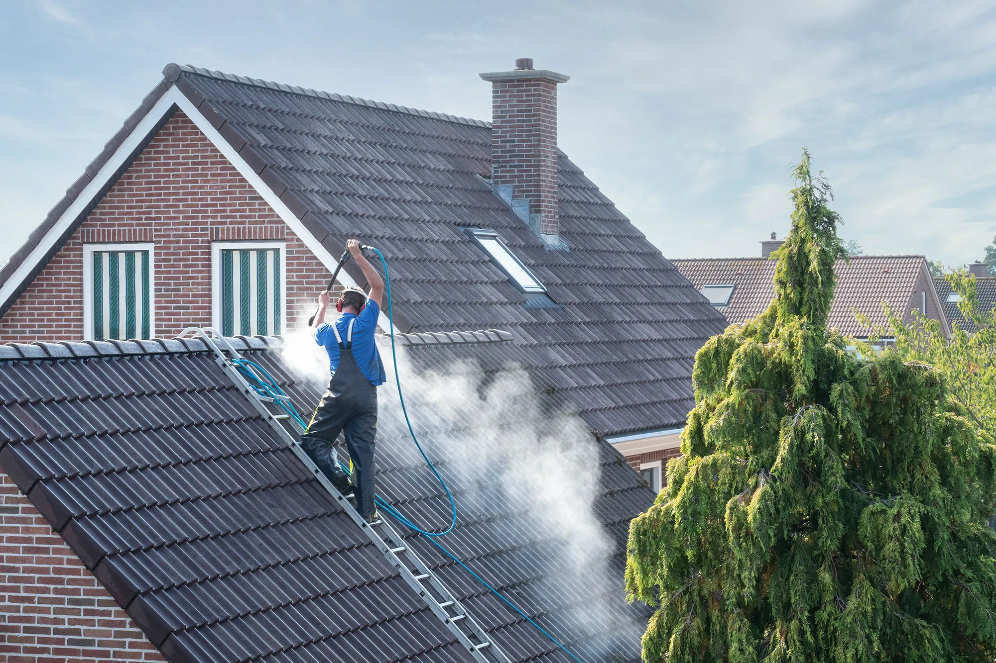 A man on a ladder cleaning the roof of a house.